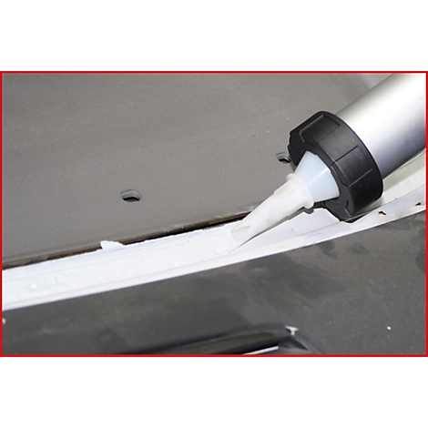 Nahaufnahme einer Silikonpistole, die weißen Kitt in eine Fuge presst. Grauer Hintergrund mit Loch.